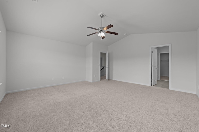 unfurnished bedroom featuring a walk in closet, baseboards, ceiling fan, light colored carpet, and lofted ceiling