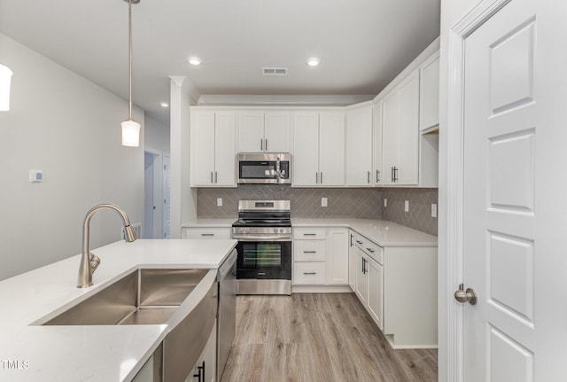 kitchen featuring light wood-type flooring, decorative backsplash, appliances with stainless steel finishes, hanging light fixtures, and a sink