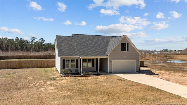 traditional-style house featuring a water view, fence, concrete driveway, a front yard, and a garage