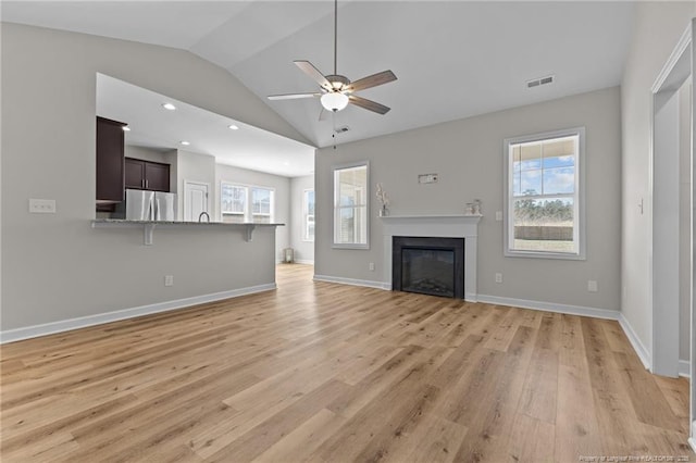 unfurnished living room with visible vents, vaulted ceiling, light wood-style floors, a glass covered fireplace, and a wealth of natural light