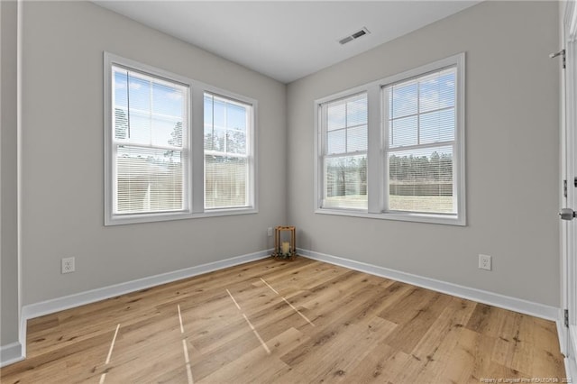 empty room with light wood-type flooring, visible vents, and baseboards