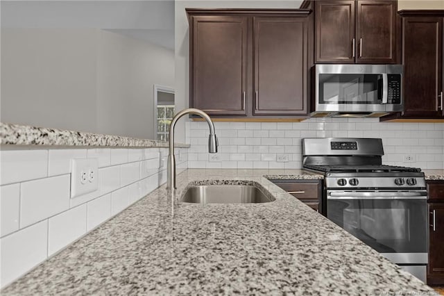 kitchen with light stone counters, dark brown cabinets, stainless steel appliances, and a sink