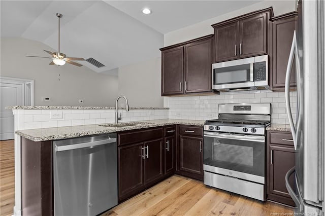 kitchen with lofted ceiling, light wood-style flooring, appliances with stainless steel finishes, a peninsula, and a sink