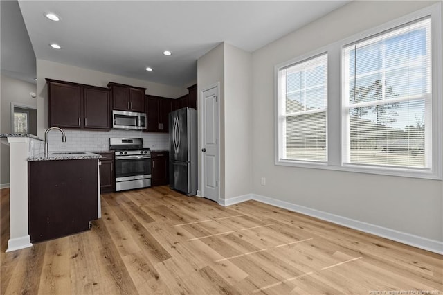 kitchen with a sink, backsplash, stainless steel appliances, baseboards, and light stone countertops