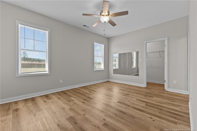 unfurnished bedroom featuring visible vents, a walk in closet, light wood-style flooring, a closet, and baseboards