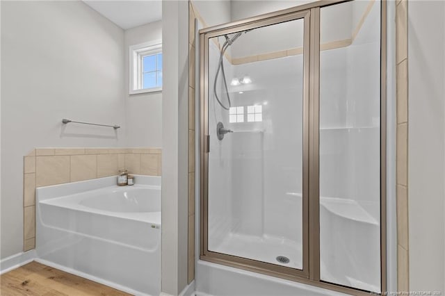 full bath featuring a shower stall, a bath, and wood finished floors