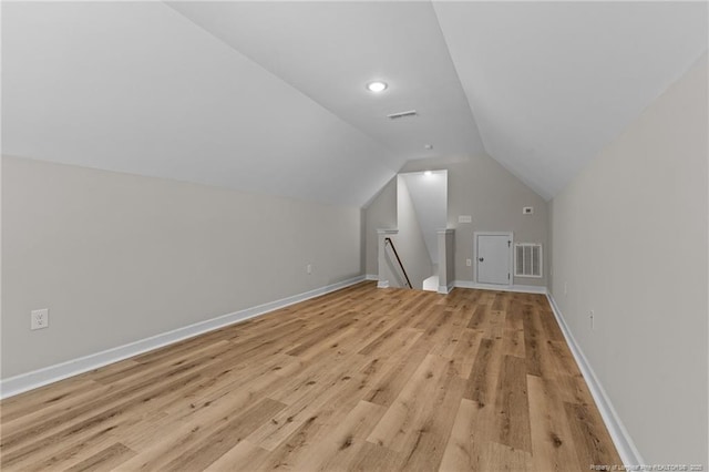 additional living space featuring vaulted ceiling, light wood-style flooring, baseboards, and visible vents