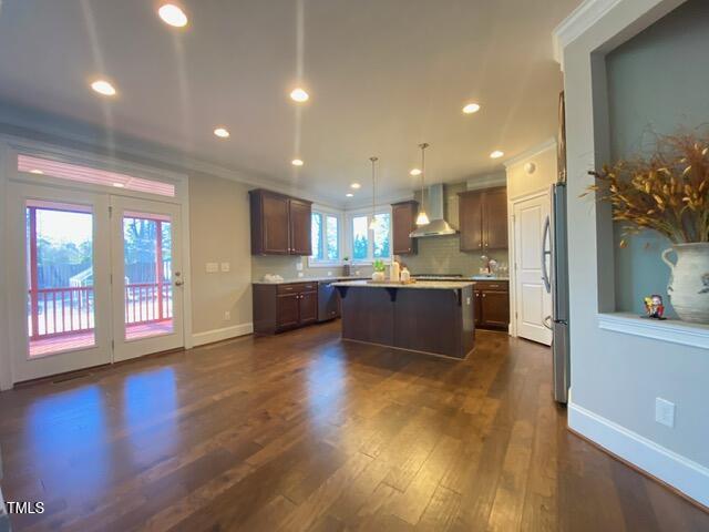 kitchen featuring a kitchen island, dark wood-type flooring, wall chimney range hood, a kitchen bar, and stainless steel appliances