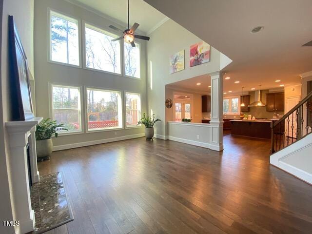 living room with dark wood-type flooring, baseboards, stairway, ornate columns, and a ceiling fan