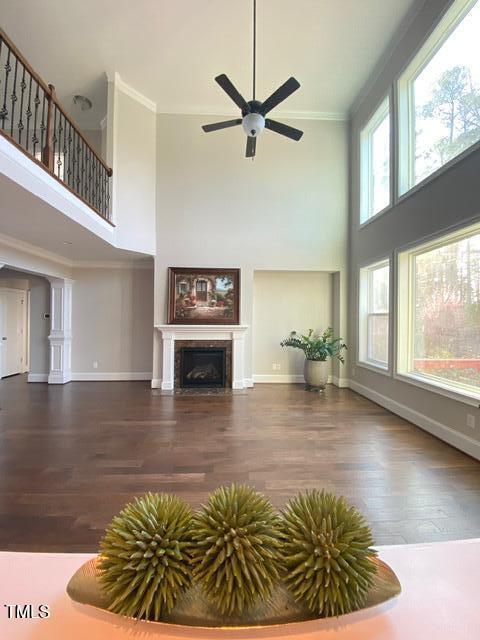 unfurnished living room with baseboards, a fireplace with flush hearth, ornamental molding, a towering ceiling, and wood finished floors