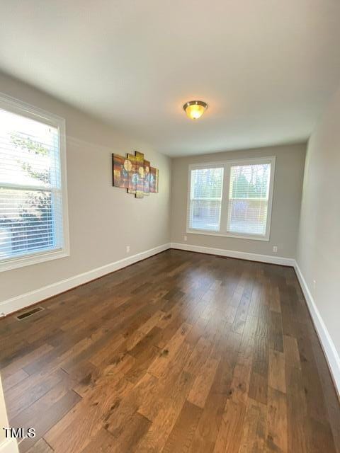 empty room with dark wood-style floors, visible vents, a healthy amount of sunlight, and baseboards