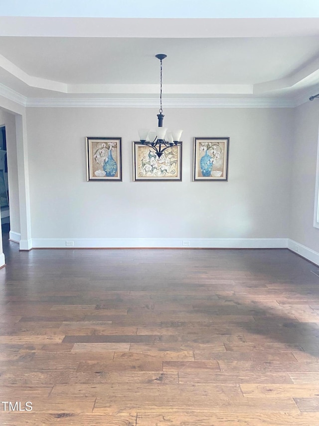 spare room featuring wood finished floors, baseboards, ornamental molding, a raised ceiling, and a chandelier