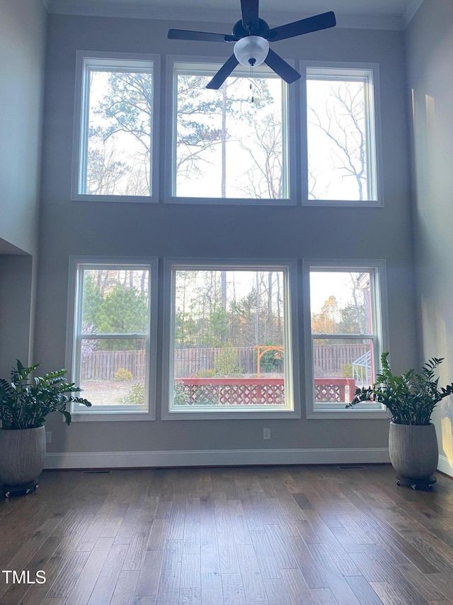 empty room with baseboards, a ceiling fan, wood finished floors, and a towering ceiling