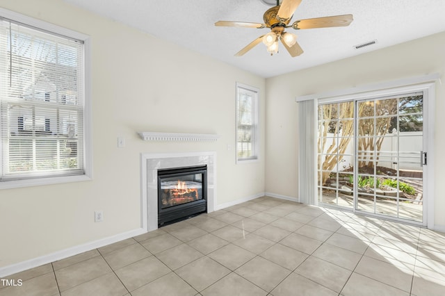 unfurnished living room featuring a glass covered fireplace, tile patterned floors, visible vents, and a wealth of natural light