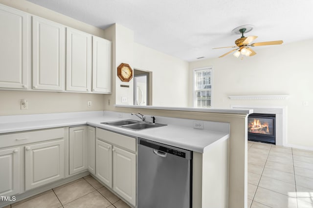 kitchen featuring a sink, a glass covered fireplace, a peninsula, light tile patterned floors, and dishwasher