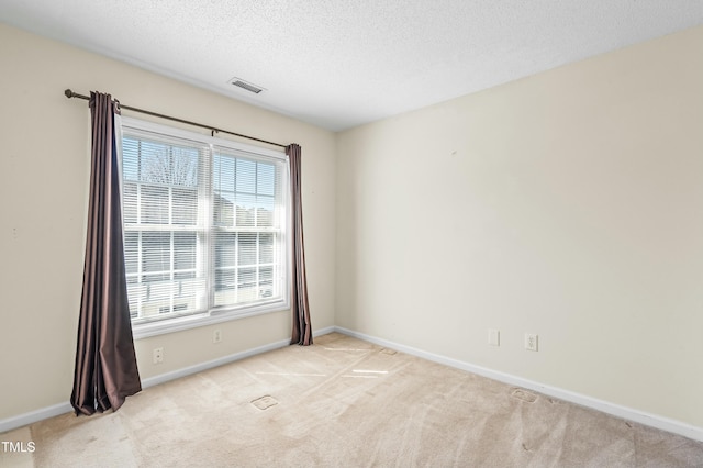 spare room featuring visible vents, light colored carpet, baseboards, and a textured ceiling