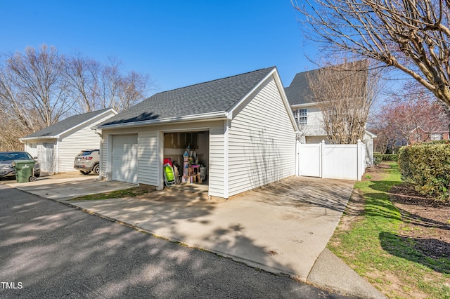 view of property exterior with a shingled roof, a detached garage, an outdoor structure, and fence