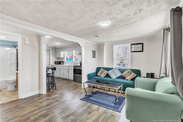 living room with a textured ceiling, ornamental molding, wood finished floors, and a wall mounted AC