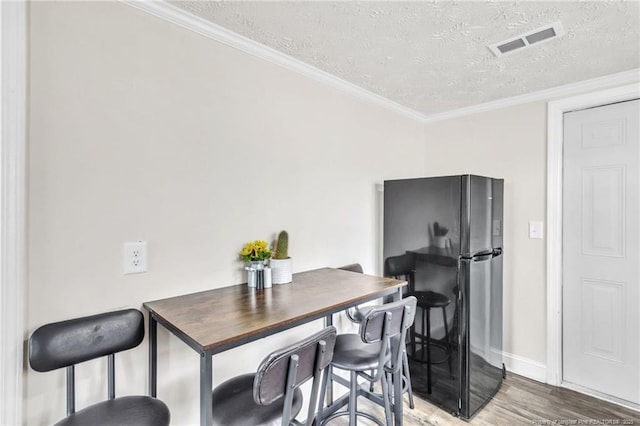 dining room featuring visible vents, baseboards, ornamental molding, wood finished floors, and a textured ceiling