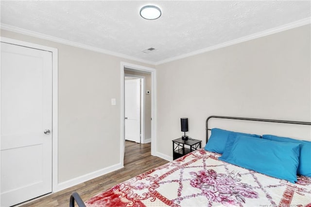 bedroom featuring ornamental molding, a textured ceiling, baseboards, and wood finished floors