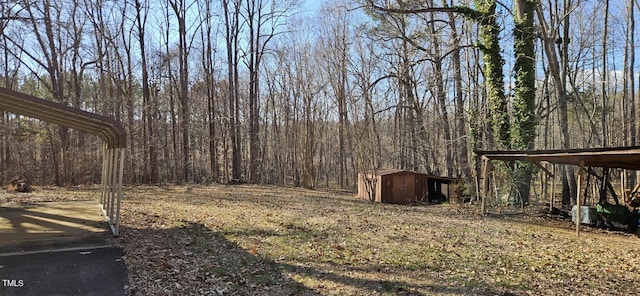 view of yard featuring a carport, a shed, a wooded view, and an outdoor structure