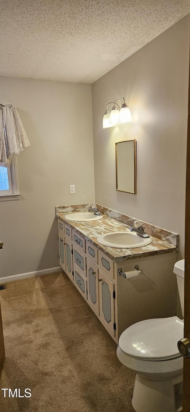 bathroom featuring a textured ceiling, double vanity, toilet, and a sink