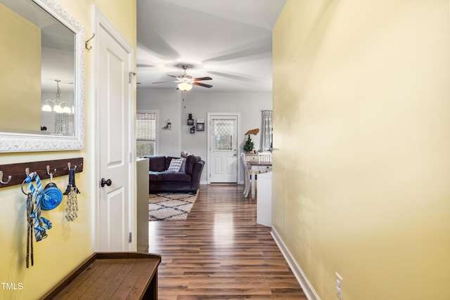 hallway featuring a chandelier, baseboards, and dark wood-style flooring