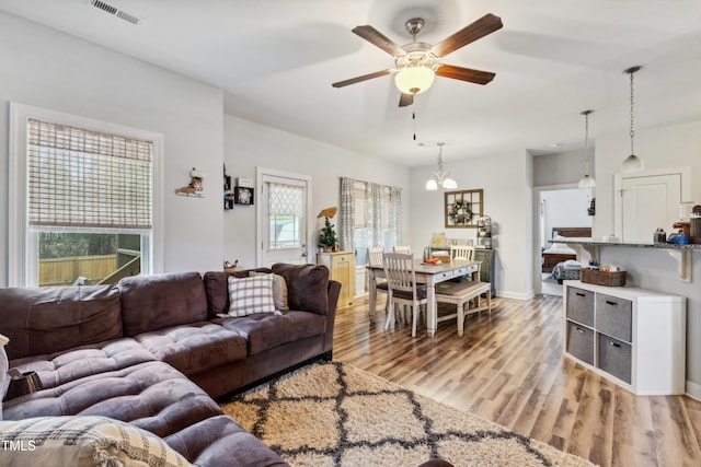 living room featuring visible vents, light wood-style flooring, ceiling fan with notable chandelier, and baseboards