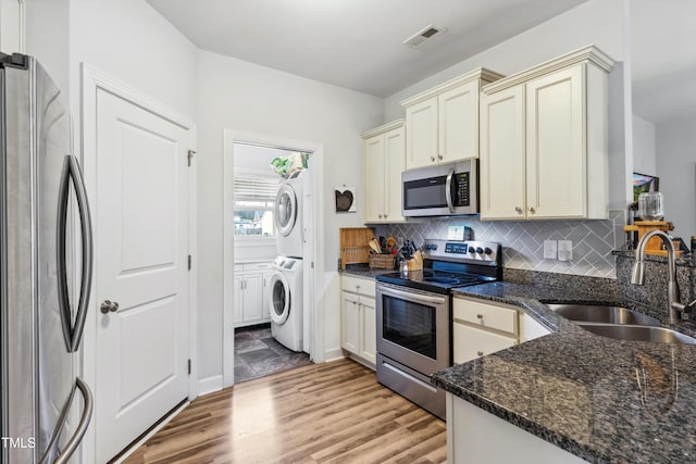 kitchen featuring stacked washing maching and dryer, a sink, appliances with stainless steel finishes, cream cabinets, and tasteful backsplash