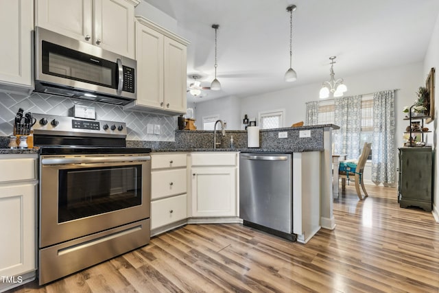 kitchen with a peninsula, a sink, light wood-style floors, appliances with stainless steel finishes, and tasteful backsplash