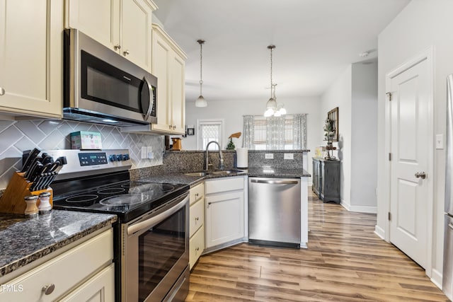 kitchen with decorative backsplash, appliances with stainless steel finishes, cream cabinets, a peninsula, and a sink