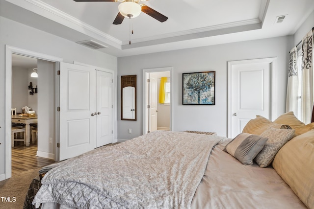 bedroom with visible vents, connected bathroom, a raised ceiling, and ornamental molding