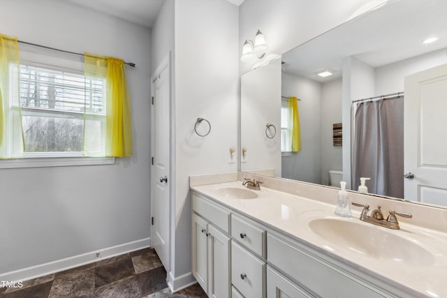 full bathroom featuring double vanity, toilet, baseboards, and a sink