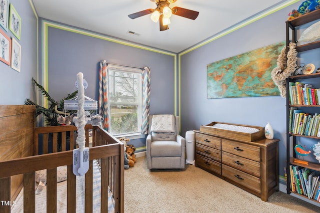 carpeted bedroom featuring visible vents, a crib, ceiling fan, and ornamental molding