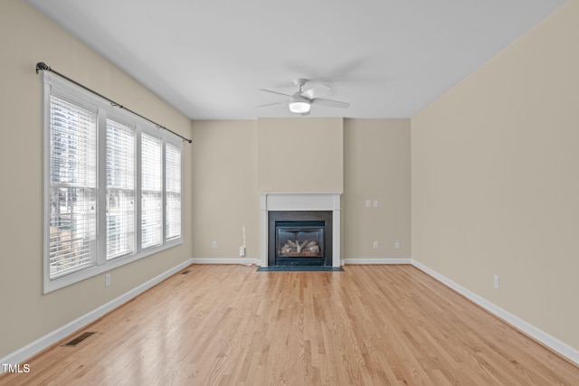 unfurnished living room with visible vents, baseboards, a fireplace with flush hearth, light wood-type flooring, and a ceiling fan