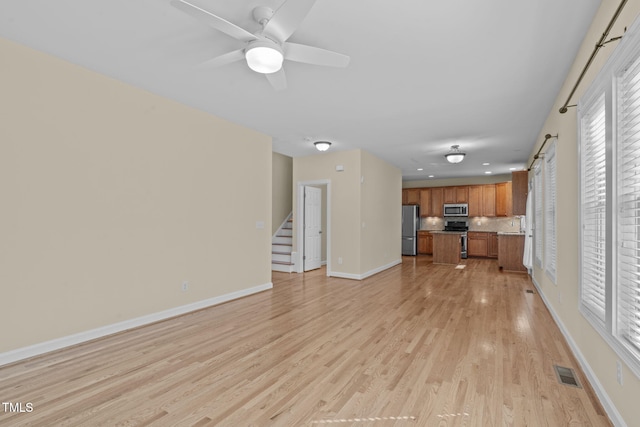 unfurnished living room featuring visible vents, stairway, light wood finished floors, baseboards, and ceiling fan