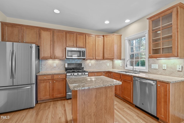 kitchen with light wood-style flooring, a sink, light stone counters, a kitchen island, and stainless steel appliances