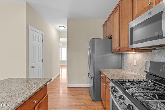 kitchen with brown cabinets, backsplash, appliances with stainless steel finishes, and light wood-style flooring