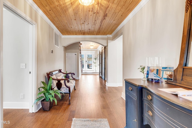 hall with visible vents, arched walkways, light wood-style floors, crown molding, and wood ceiling