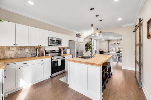 kitchen featuring arched walkways, butcher block countertops, stainless steel appliances, and a sink