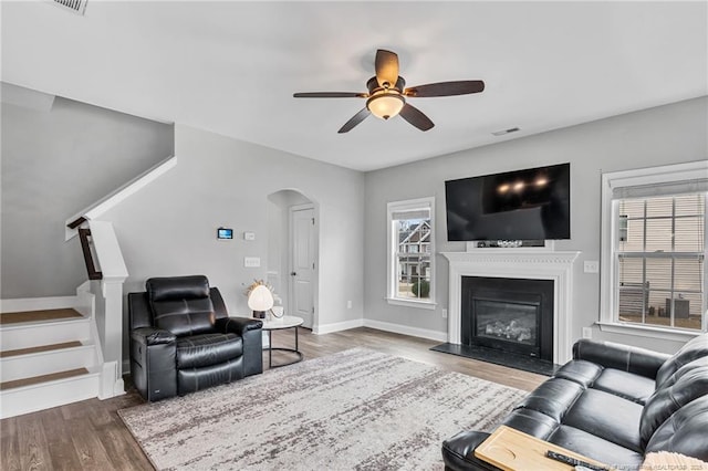 living area with visible vents, a glass covered fireplace, wood finished floors, arched walkways, and stairs