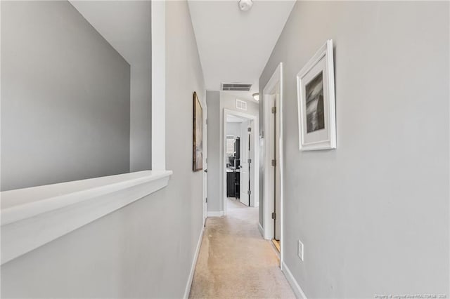 corridor featuring visible vents, baseboards, and light colored carpet