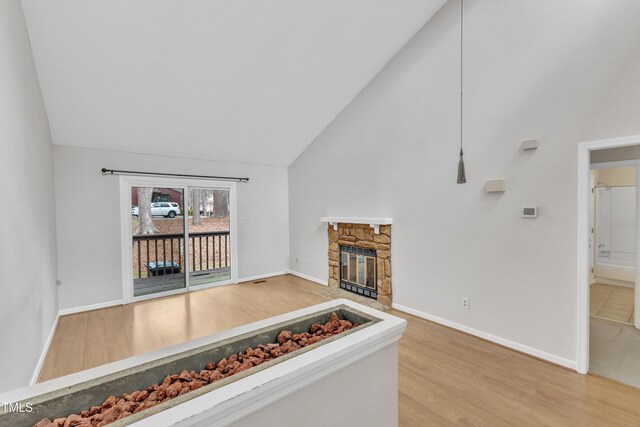 unfurnished living room featuring a stone fireplace, wood finished floors, baseboards, and high vaulted ceiling