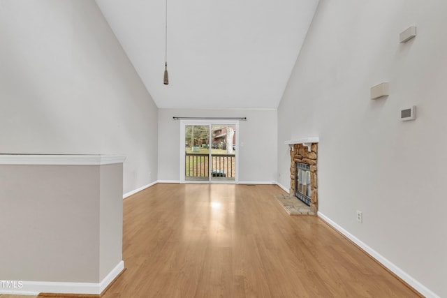 unfurnished living room with light wood-type flooring, baseboards, high vaulted ceiling, and a fireplace