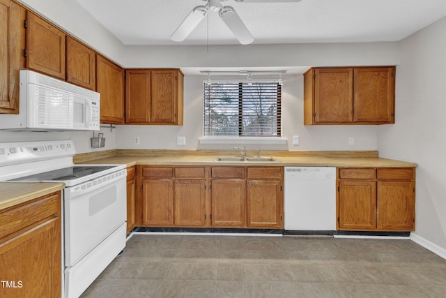 kitchen featuring white appliances, a ceiling fan, brown cabinetry, a sink, and light countertops