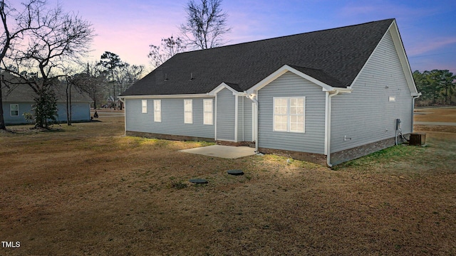 back of house at dusk featuring a yard, central AC unit, and a shingled roof