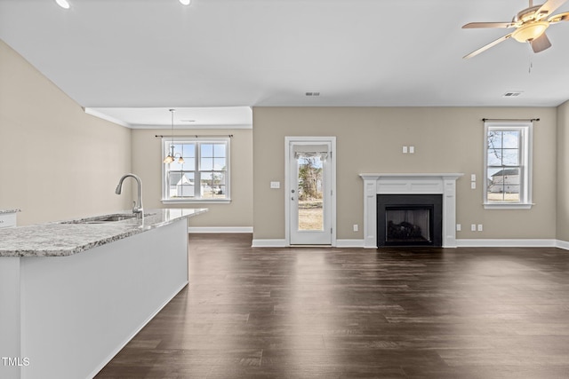 unfurnished living room with dark wood-style flooring, baseboards, a ceiling fan, and a sink