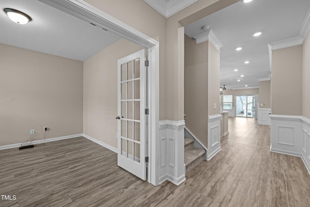 corridor featuring a wainscoted wall, ornamental molding, recessed lighting, wood finished floors, and a decorative wall