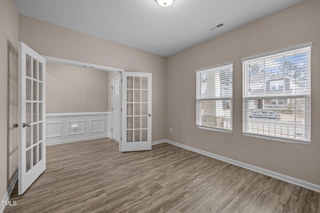 spare room featuring a wainscoted wall, visible vents, wood finished floors, french doors, and a decorative wall