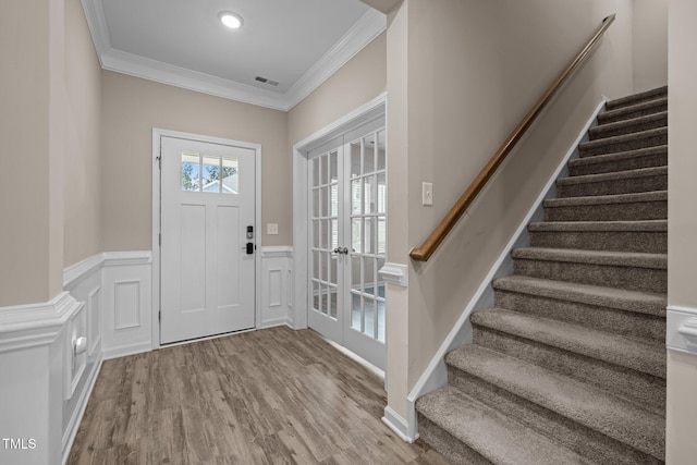 entrance foyer featuring visible vents, ornamental molding, wood finished floors, wainscoting, and stairs